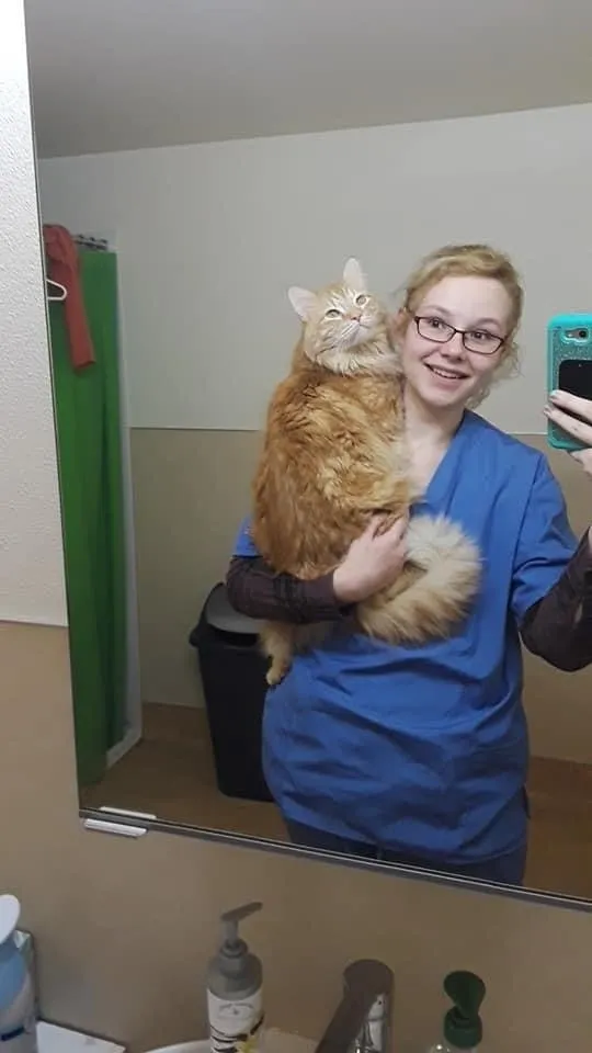 A woman holding an orange cat in her arms.